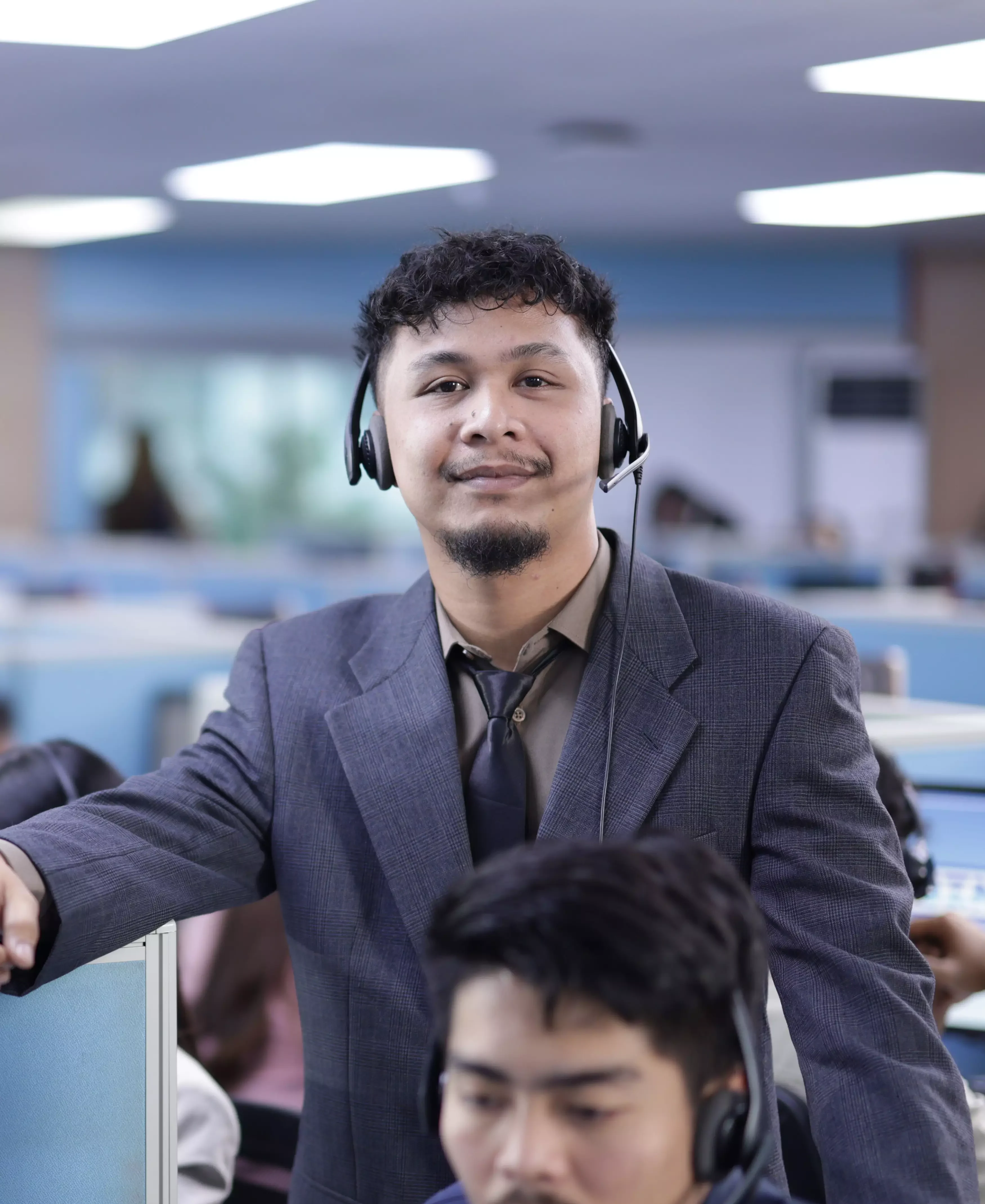 Male employee standing and smiling with a headset, while looking at the camera in the workplace.